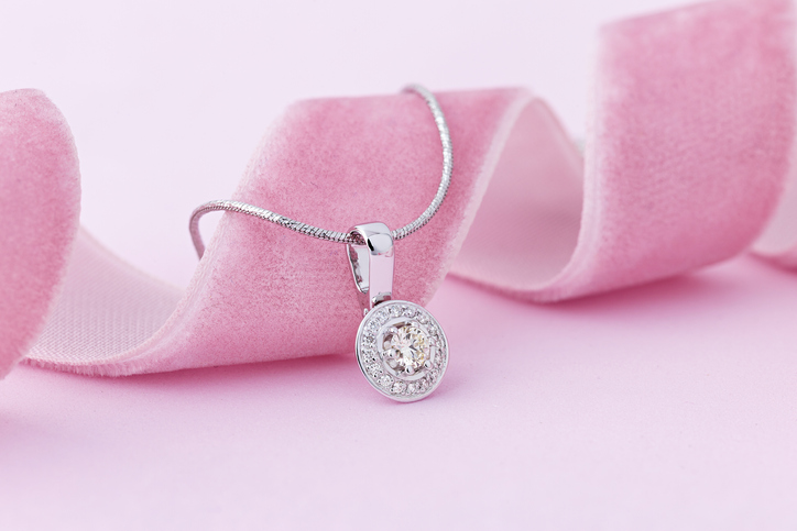 Elegant white gold necklace with diamonds on pastel pink background. Small silver charm necklace with gemstones for romantic occasion