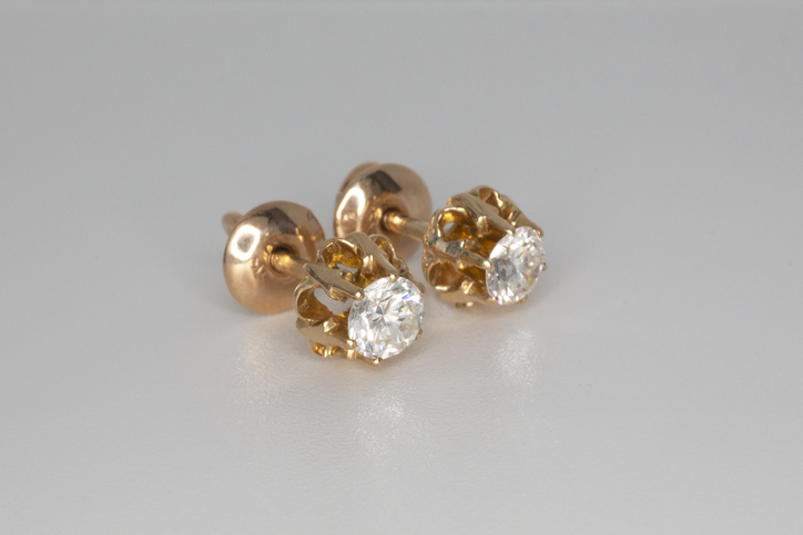 Close-up of gold stud earrings with white crystals and diamonds. Beautiful yellow gold earrings on a gray background. Women's accessories